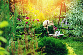 A peaceful scene of a wooden chair with a straw hat on the back in a secluded green well-planted area of a garden